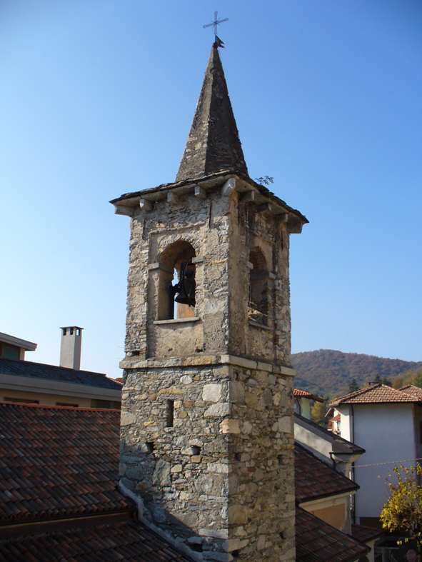 Parte alta di un campanile antico con la sede delle campane e il tetto piramidale che termina con la croce.