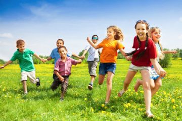 Sette bambini che corrono su un prato fiorito.