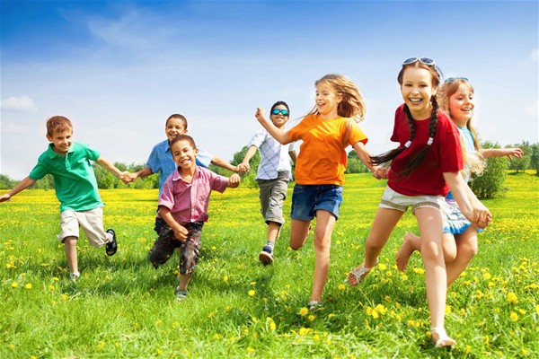 Sette bambini che corrono su un prato fiorito.