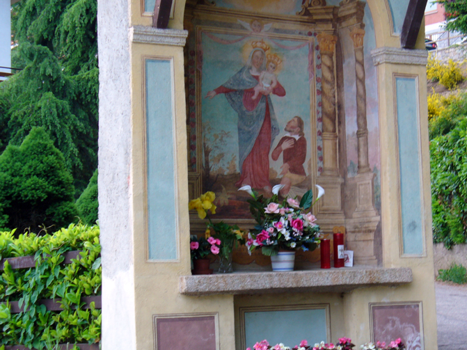 Cappelletta con frontale dipinto di azzurro e raffigurazione della Madonna con Bambino e uomo in ginocchio.