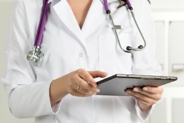 Una dottoressa in camice bianco con lo stetoscopio intorno al collo ed in mano una cartellina.