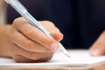 Una mano destra che impugna una penna biro per firmare un documento.