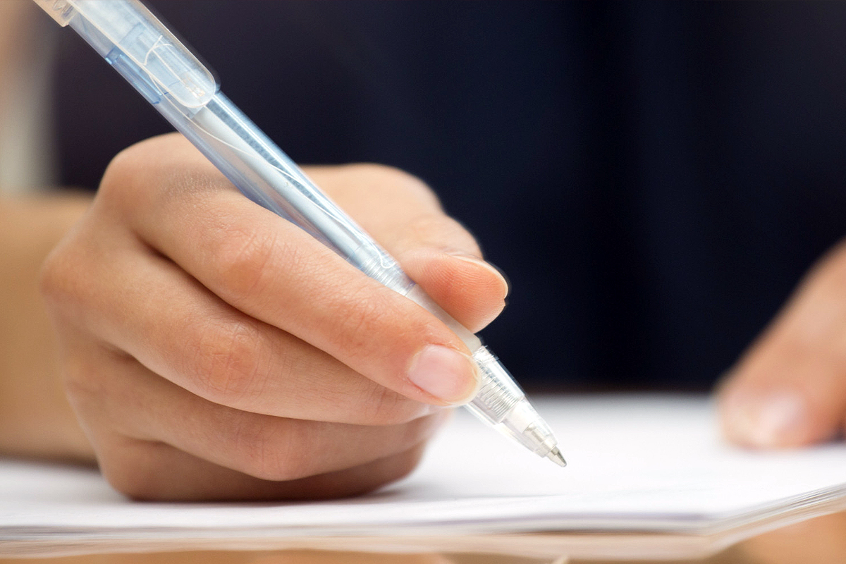 Una mano destra che impugna una penna biro per firmare un documento.