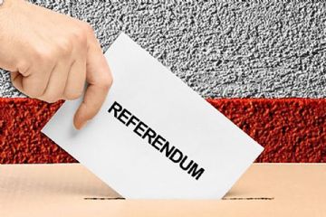 Una mano che inserisce in un'urna elettorale la scheda di votazione recante la scritta "Referendum".