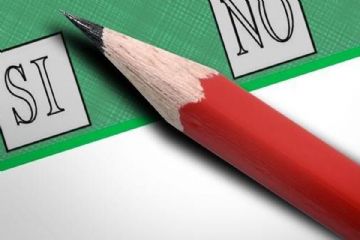 Una matita rossa posata su una scheda di votazione verde tra le caselle Sì e No.