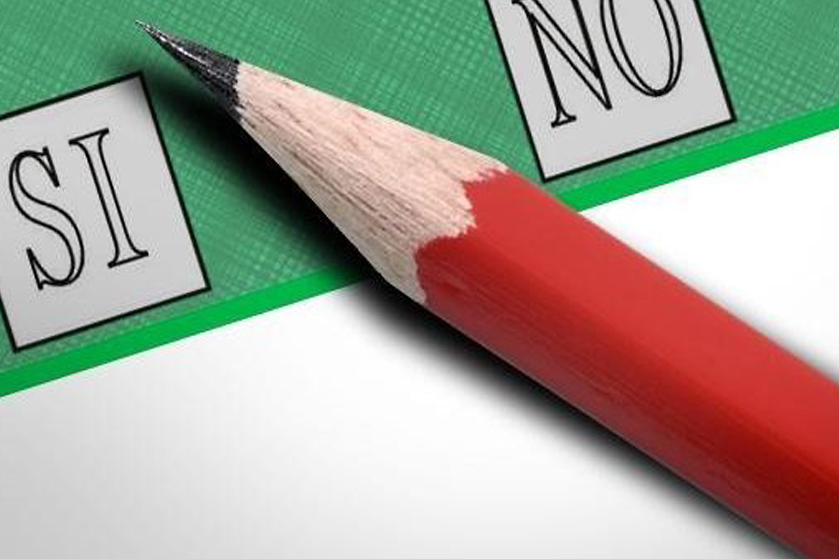 Una matita rossa posata su una scheda di votazione verde tra le caselle Sì e No.