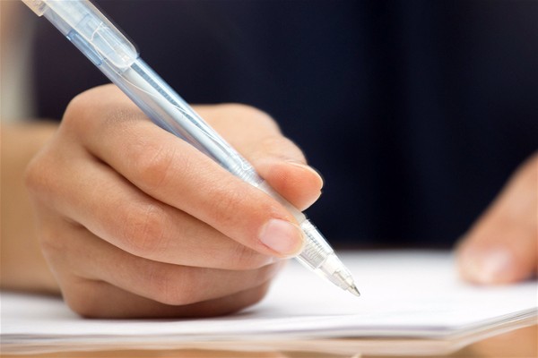 In primo piano una mano firma un foglio bianco con una penna biro.